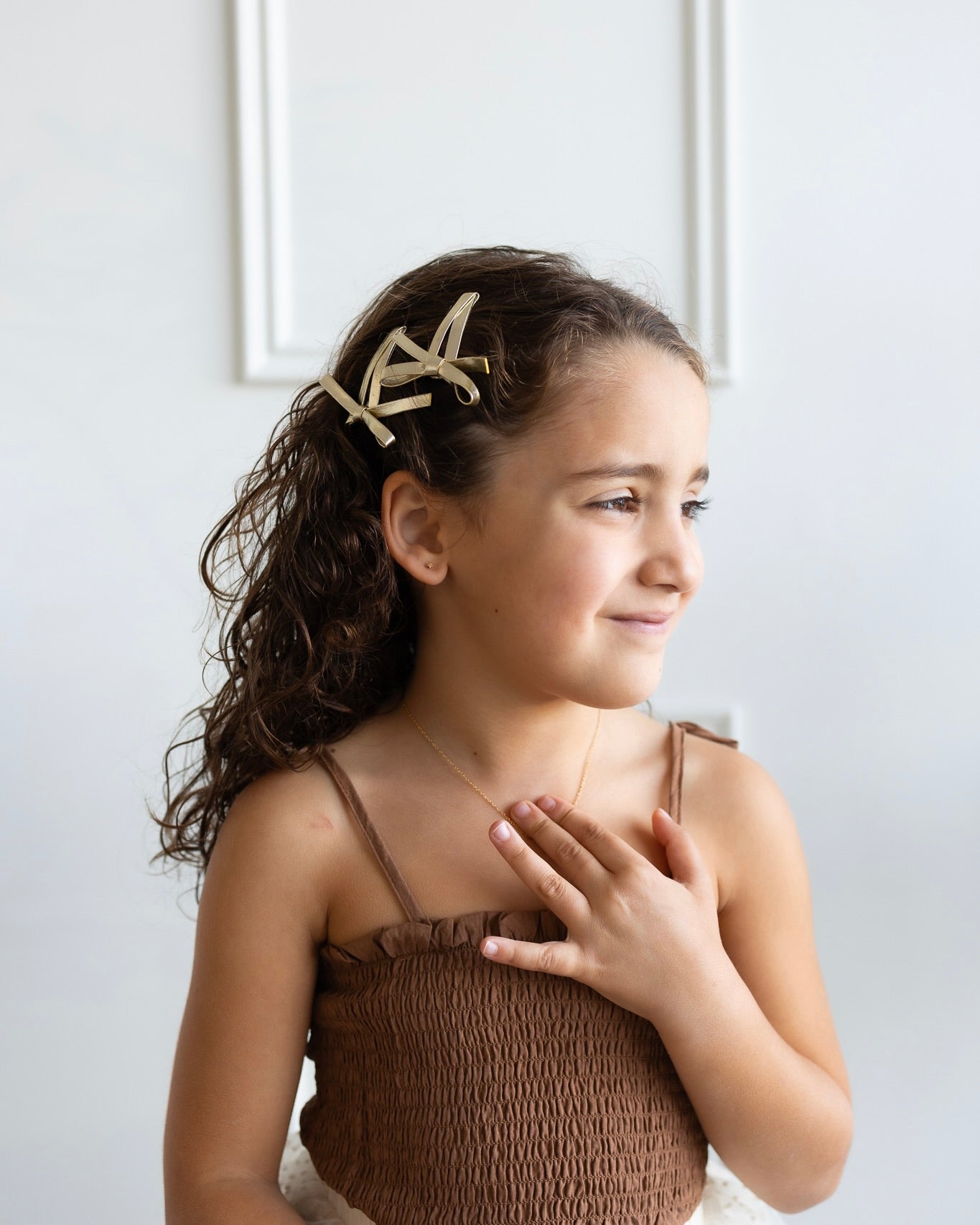 Child wearing a gold bow hair clip and delicate kids jewelry, soft and timeless accessories for children